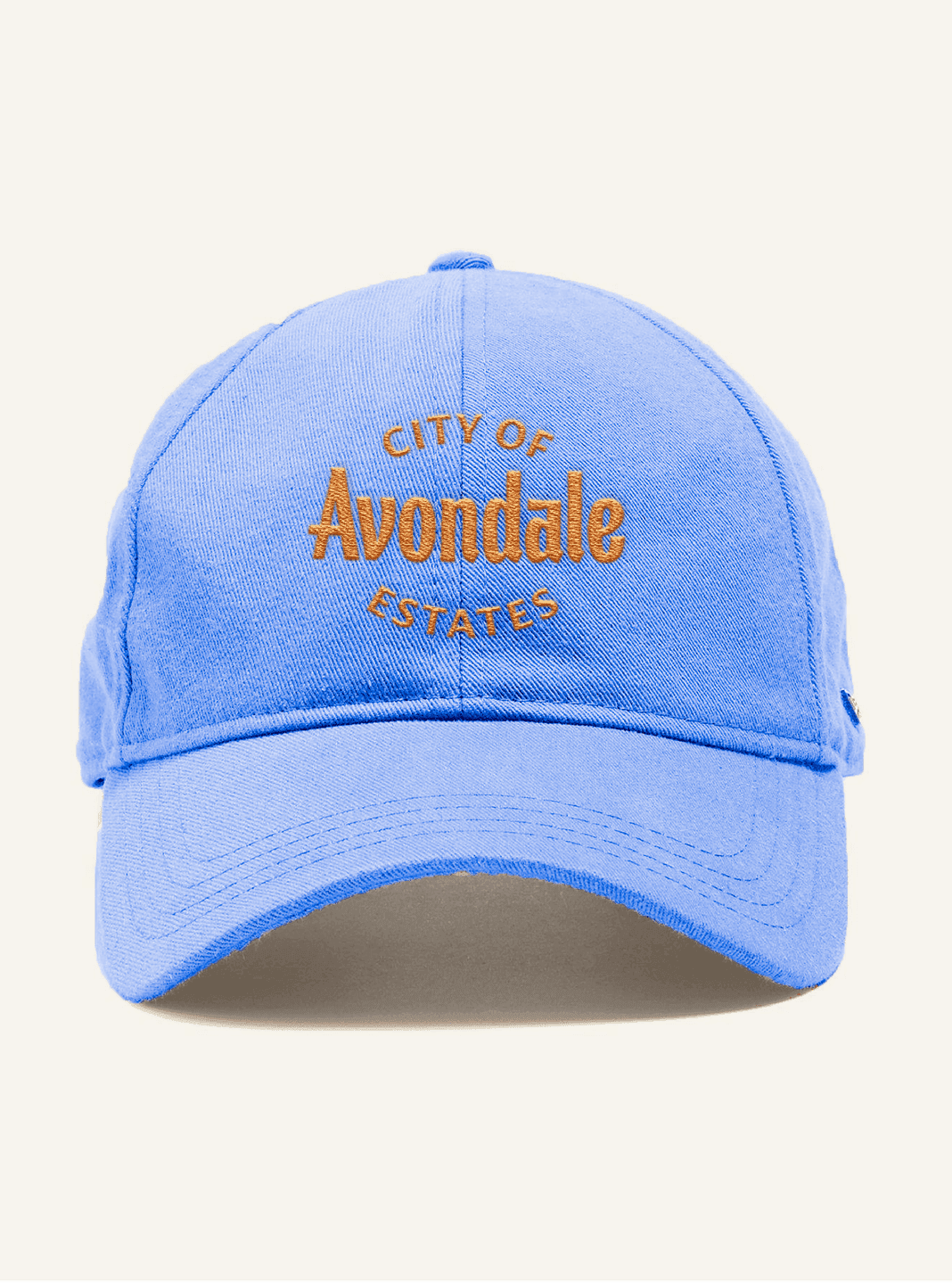 A light blue baseball cap features the embroidered “City of Avondale Estates” seal in orange stitching