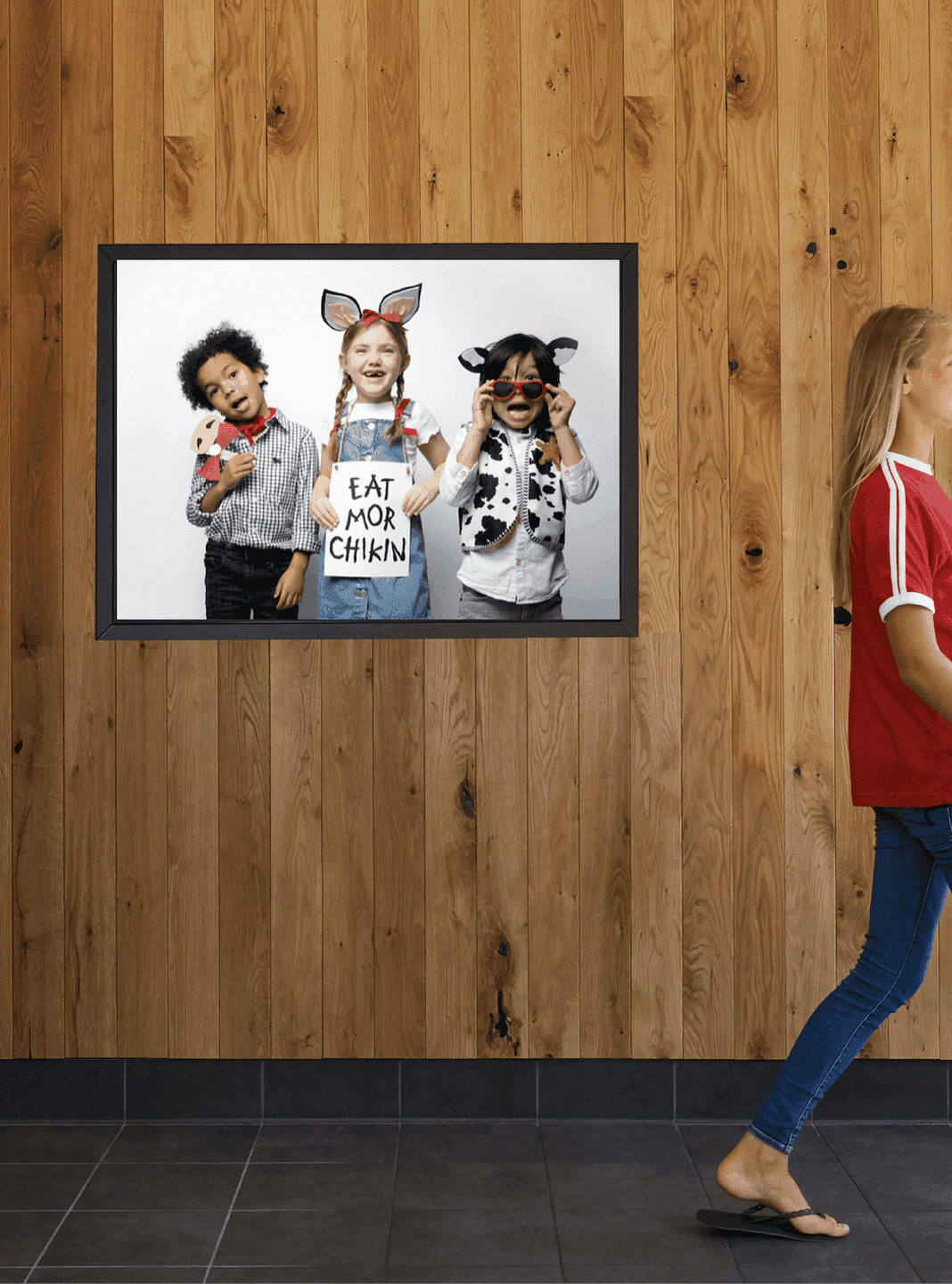 Kids in Cow-Themed Photo Booth. Three children pose in cow-themed costumes holding an “Eat Mor Chikin” sign against a wooden wall backdrop.