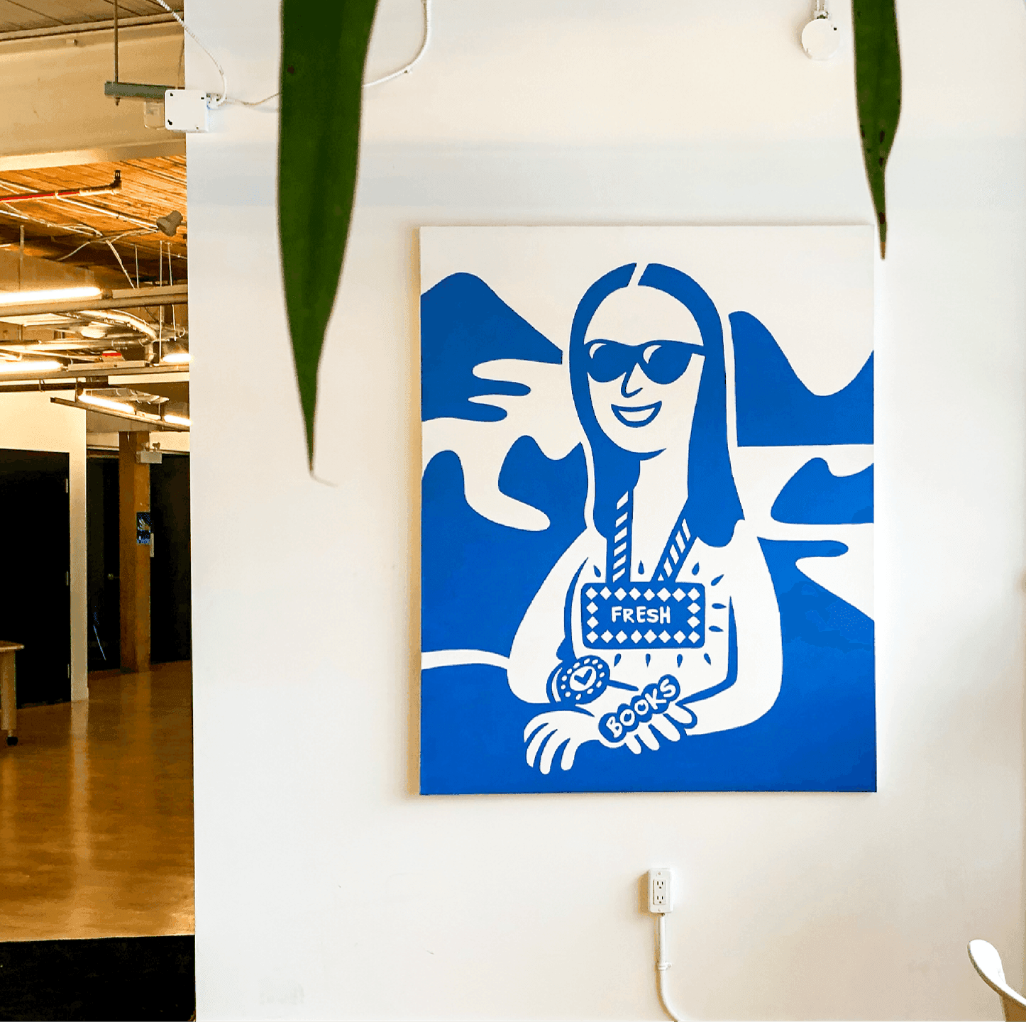 Office Mural. A large blue-and-white mural of a stylized character wearing a FreshBooks badge displayed inside the office.